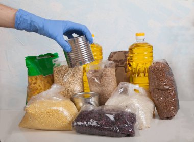 Yiyecek bağışı. Eldiven giyen bir erkek, beyaz arka planda bir dizi ürün bağışına teneke kutu koyar. sosyal yardım