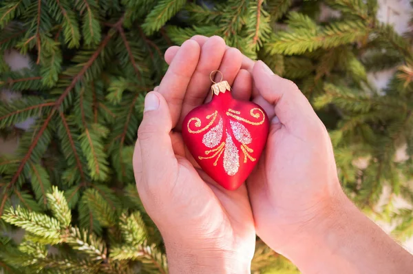 Brinquedo de Natal em forma de coração vermelho nas mãos — Fotografia de Stock