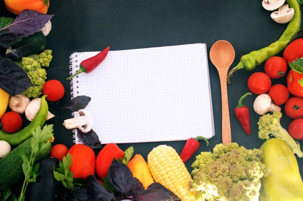 Blocco note, verdure fresche e cucchiaio su sfondo nero — Foto Stock