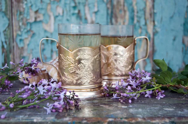 Two glasses of tea in cup holders and ablossoming lilac next to — Stock Photo, Image