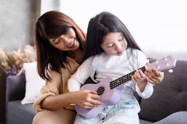 Anne güzel kızıyla ukulele öğretiyor, stüdyo müzik odasında, aile aktivitelerinde, mutlu bir şekilde.