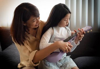 Anne güzel kızıyla ukulele öğretiyor, stüdyo müzik odasında, mutlu aile rahatlama zamanı,