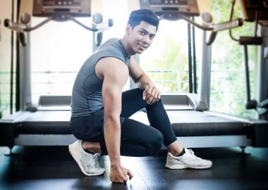 Yakışıklı adam zemin katta diz çöker, zemin katta yumruk tokuşturur, egzersize hazırlan, spor salonunda, sağlık merkezinde, bulanık ışık etrafında.