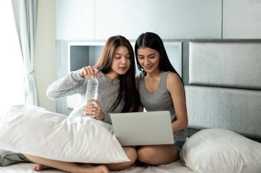 Yatakta oturan, su içen, dizüstü bilgisayar kullanan, birlikte aktiviteler yapan güzel kadınlar. Mutlu bir duygu, iyi bir an, romantik bir aşk çifti, en iyi arkadaşlık.