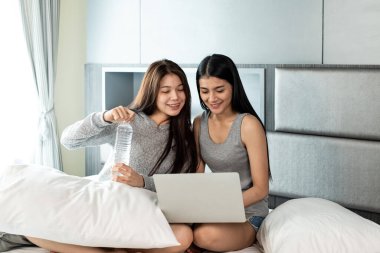 Yatakta oturan, su içen, dizüstü bilgisayar kullanan, birlikte aktiviteler yapan güzel kadınlar. Mutlu bir duygu, iyi bir an, romantik bir aşk çifti, en iyi arkadaşlık.