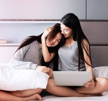 Yatakta oturan güzel kadınlar, dizüstü bilgisayar kullanıyorlar, konuşuyorlar, birlikte hareket ediyorlar.,