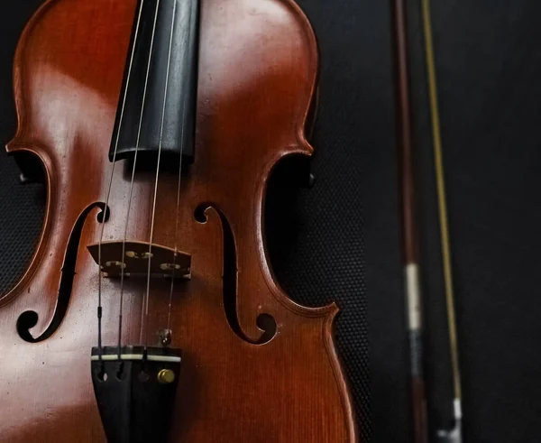 黒いキャンバスの上にぼんやりとした弓の横に置かれたバイオリンの閉じ込められたフロント側 周りのぼやけた光 — ストック写真