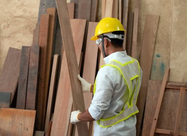 Güvenlik yeleği ve sarı kask giyen, kereste tahtasını seçen, fabrikada ahşap işi yapan, el yapımı...