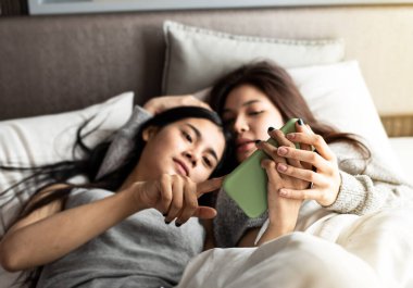 Cep telefonunun seçici odak noktasında iki eli aşk tutuyordu. Romantik duygularla iki kadını yatağa uzanmış şekilde bulanıklaştırıyordu..