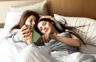 Cep telefonunun seçici odak noktasında iki eli aşk tutuyordu. Romantik duygularla iki kadını yatağa uzanmış şekilde bulanıklaştırıyordu..