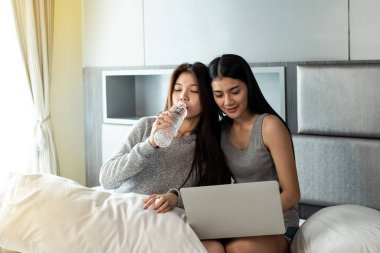 Yatakta oturan, su içen, dizüstü bilgisayar kullanan, birlikte aktiviteler yapan güzel kadınlar. Mutlu bir duygu, iyi bir an, romantik bir aşk çifti, en iyi arkadaşlık.