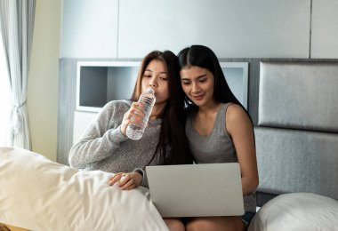 Yatakta oturan, su içen, dizüstü bilgisayar kullanan, birlikte aktiviteler yapan güzel kadınlar. Mutlu bir duygu, iyi bir an, romantik bir aşk çifti, en iyi arkadaşlık.