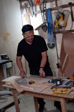 Koruyucu gözlük takan yakışıklı adam, fabrikada ahşap işi yapan, el yapımı tasarım yapan, marangoz.