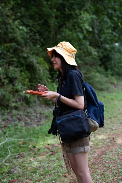 年轻的女士戴着黄色的帽子 在书上写着字 在路上探索 在森林里 周围的光线模糊不清 — 图库照片