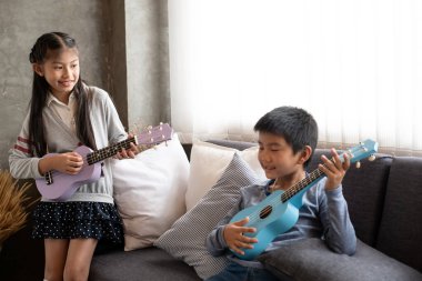 Görme engelli çocuk kanepede arkadaşıyla ukulele oynuyor. Ev stüdyosunda, bulanık bir ışık.