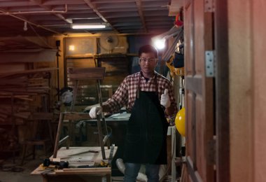 Koruyucu gözlük takan yakışıklı adam, ayağa kalk ve gülümse, başarı için el yapımı ahşap tasarımı, ev stüdyosunda, Lens ışığı, bulanık ışık