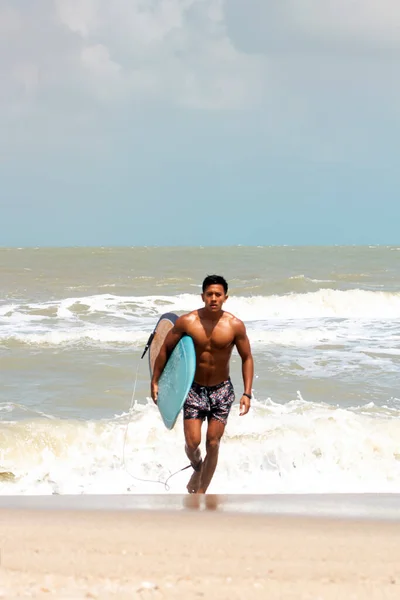 Young handsome man wet all over body holding surfboard with right hand,walking on the beach,show fit and firm body,model posing,blurry light around