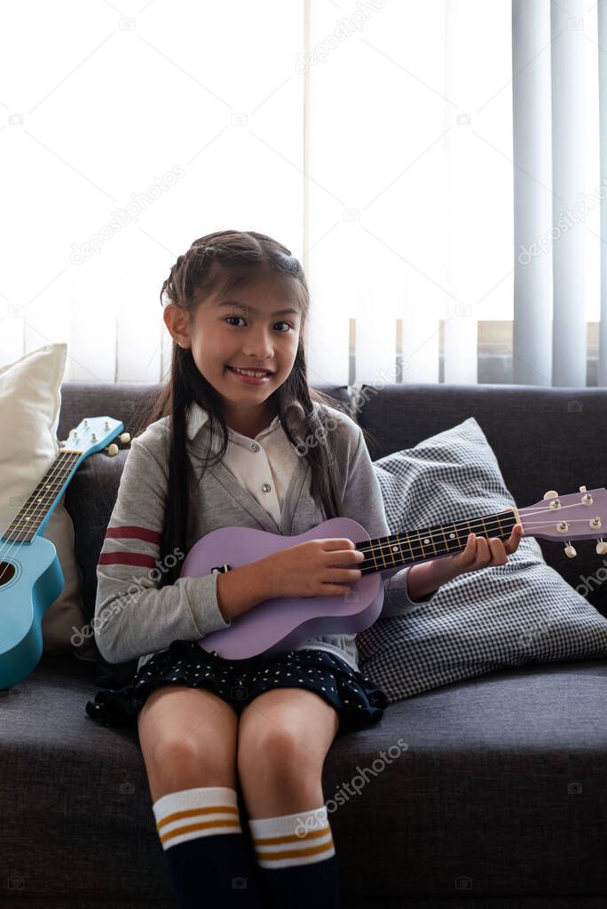 The little girl sitting on sofa,playing ukulele with happy feeling,blurry light around