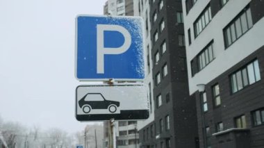 Road sign blue color of the pointer of the parking lot. Allowed parking place. Snowfall, cloudy gray sky, winter after heavy snow, after a storm 