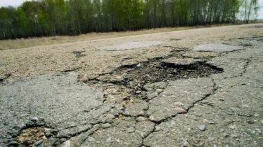 A large pit on the road. Cracked ruined asphalt pit roads, panning shot in sunny summer day.