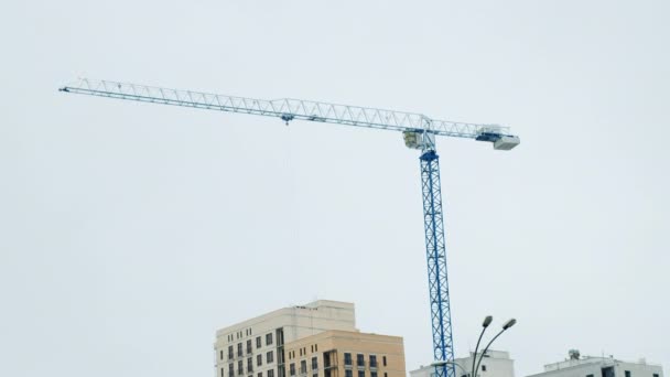 Crane Working on Construction Site Under Grey Cloudy Sky on a Rainy Day. Construction process of skyscraper and new apartments with blue crane. Construction in downtown of the big city. — стоковое видео