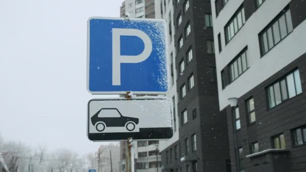 Road sign blue color of the pointer of the parking lot. Allowed parking place. Snowfall, cloudy gray sky, winter after heavy snow, after a storm — Stok video