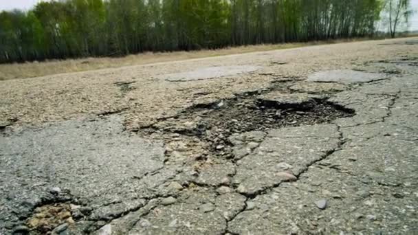 A large pit on the road. Cracked ruined asphalt pit roads, panning shot in sunny summer day. — Wideo stockowe