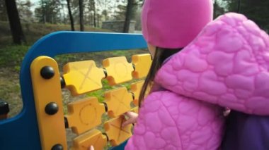 A schoolgirl plays at the school site in cool weather. The child solves a logical exercise. Adorable girl has fun at playground.