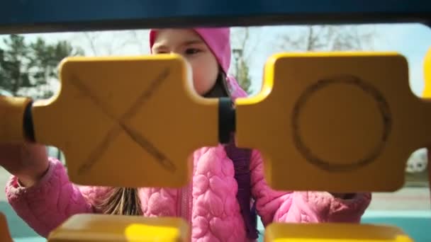 Šťastná holčička si hraje na hřišti v chladném počasí. Dítě řeší logické cvičení. Rozkošná dívka se baví na hřišti. — Stock video