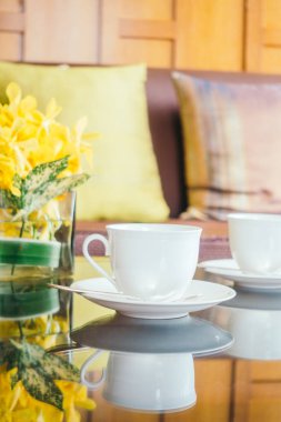 Vazo çiçek ve beyaz kahve fincanı masada ve kanepe yastık