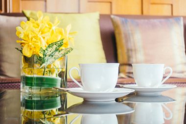 Vazo çiçek ve beyaz kahve fincanı masada ve kanepe yastık