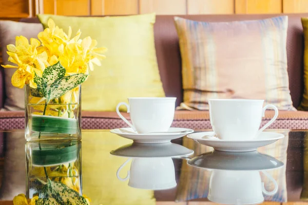 Vazo çiçek ve beyaz kahve fincanı masada ve kanepe yastık