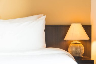 Yatak odasının içinde lamba süslemesi olan beyaz rahat bir yastık.