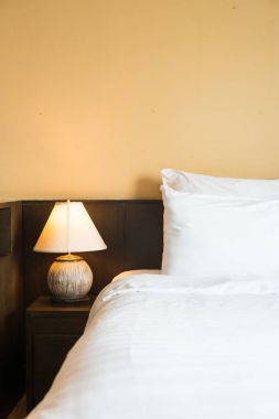 Yatak odasının içinde lamba süslemesi olan beyaz rahat bir yastık.