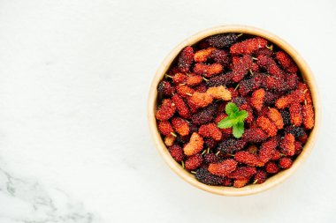 Kırmızı ve siyah dut meyve kase beyaz taş zemin üzerine