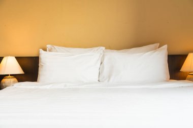 Yatak odasının içinde lamba süslemesi olan beyaz rahat bir yastık.