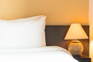 Yatak odasının içinde lamba süslemesi olan beyaz rahat bir yastık.