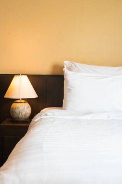 Yatak odasının içinde lamba süslemesi olan beyaz rahat bir yastık.