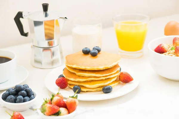 Healthy Breakfast set with Pancake and Granola with blueberry and strawberry and black coffee , Milk and Orange juice on white stone table background