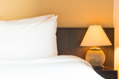 Yatak odasının içinde lamba süslemesi olan beyaz rahat bir yastık.