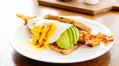 Avokado bacon ve beyaz tabak içinde kuşkonmaz ile sandviç