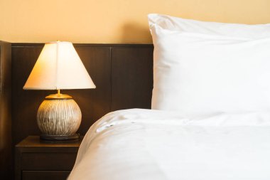 Yatak odasının içinde lamba süslemesi olan beyaz rahat bir yastık.