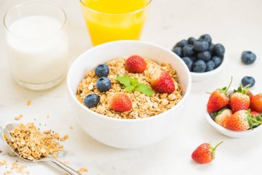 Sağlıklı kahvaltı Granola yaban mersini ve çilek ve siyah kahve, süt ve portakal suyu ile beyaz taş tablo arka planı ayarla