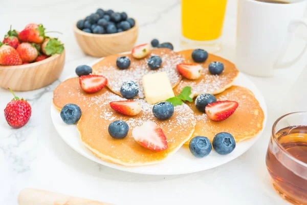 Healthy Breakfast set with Pancake blueberry and strawberry fruits and black coffee , Milk and Orange juice on white stone table background