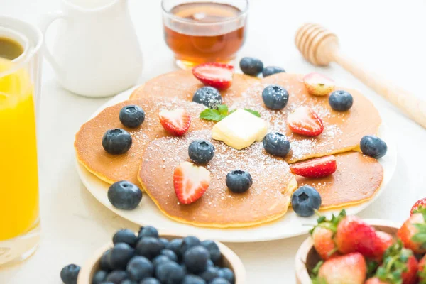 健康早餐配有煎饼蓝莓和草莓水果 黑咖啡 牛奶和橙汁在白色的石头桌背景 — 图库照片