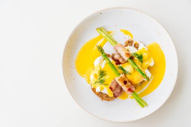 Pastırmalı yumurta benedict kuşkonmaz beyaz tabak içinde twist.