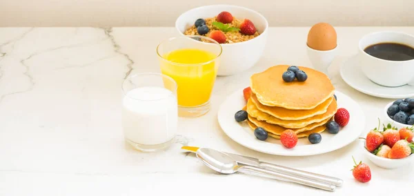 Healthy Breakfast set with Pancake and Granola with blueberry and strawberry and black coffee , Milk and Orange juice on white stone table background