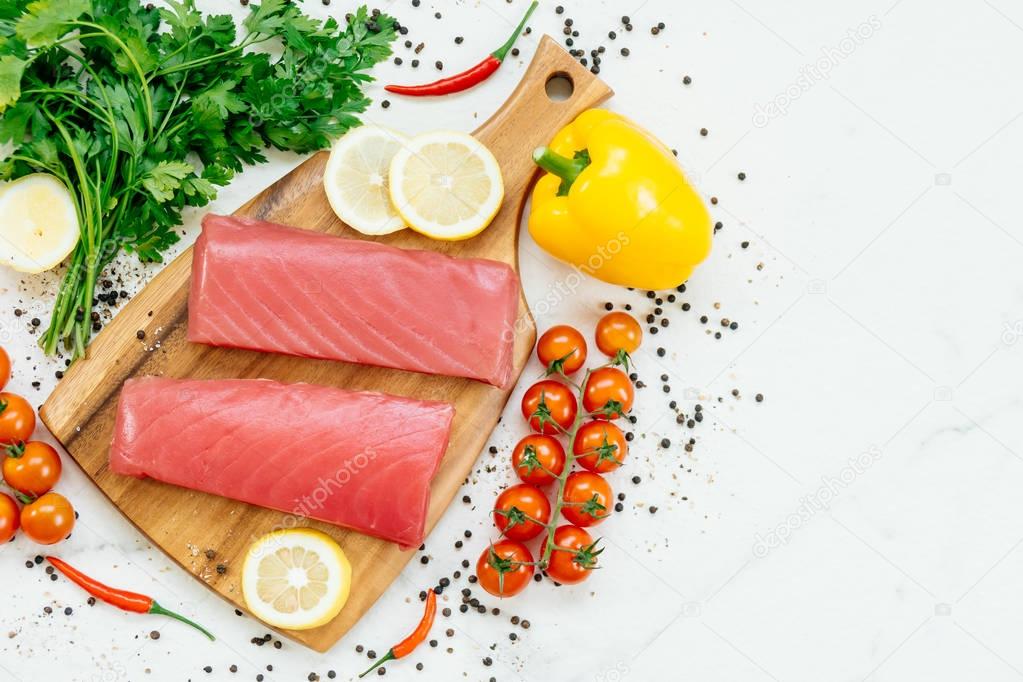 Raw tuna fish fillet meat on wooden cutting board with vegetable and ingredient for cooking