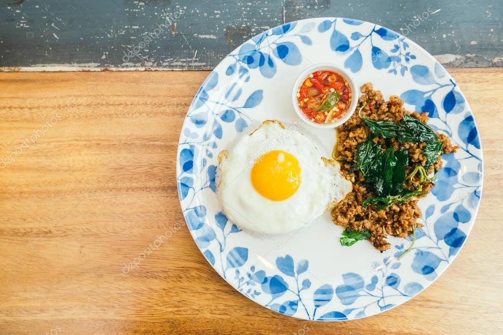 Spicy pork with basil leaf and rice on top with fried eggs in plate - Thai food style