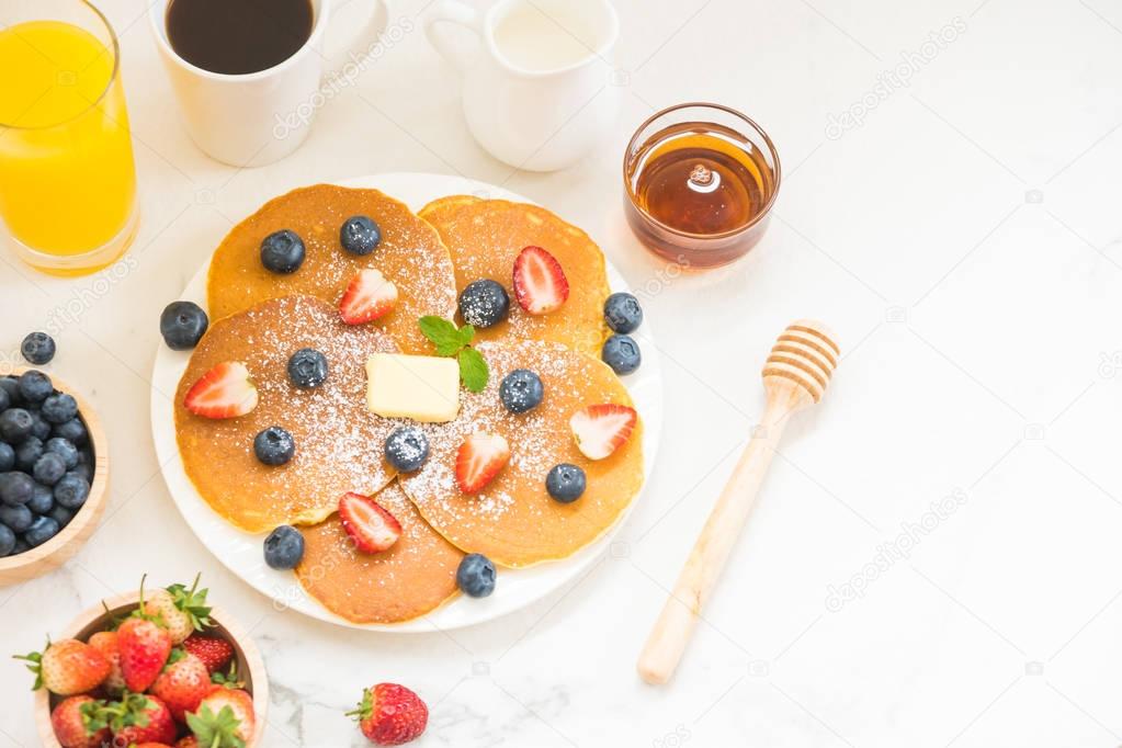 Healthy Breakfast set with Pancake blueberry and strawberry fruits and black coffee , Milk and Orange juice on white stone table background